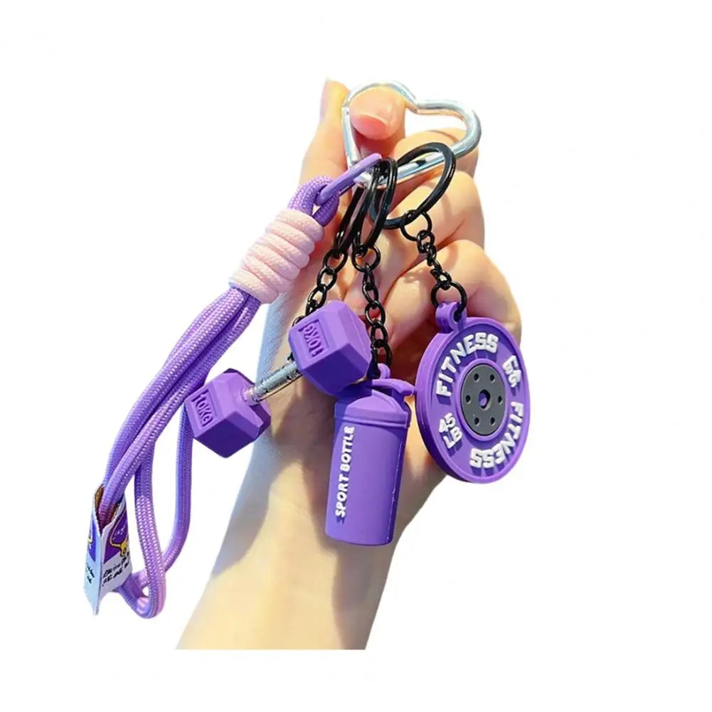 A hand holds a purple fitness keychain featuring a dumbbell and kettlebell charm.