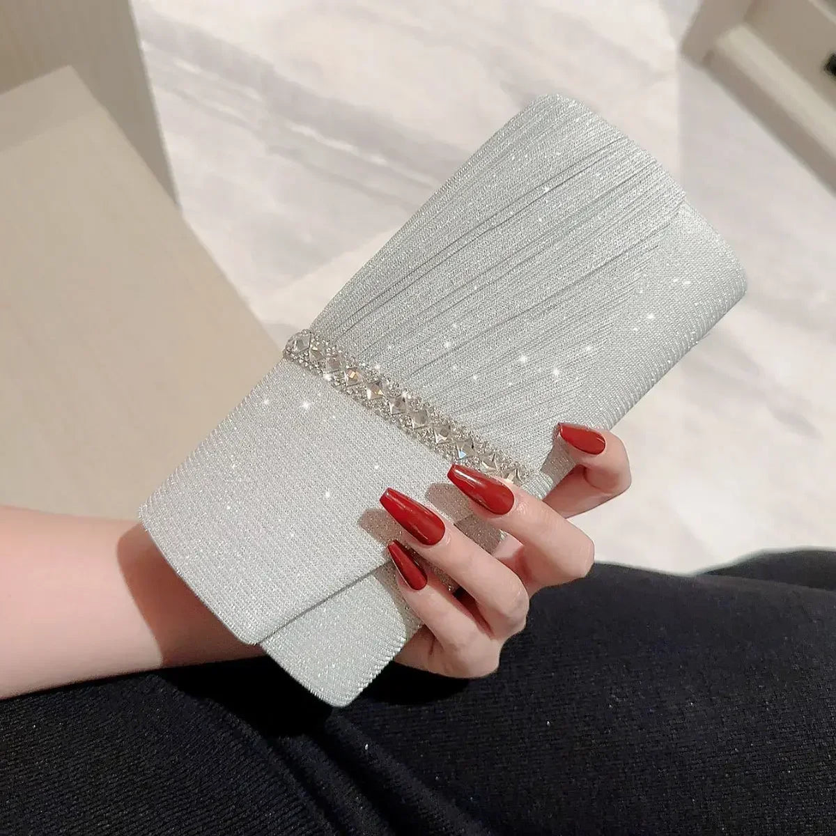 Eine Hand hält eine elegante silberne Halskette als Schultertasche mit Glitzerstruktur und silberner Kettendetail.
