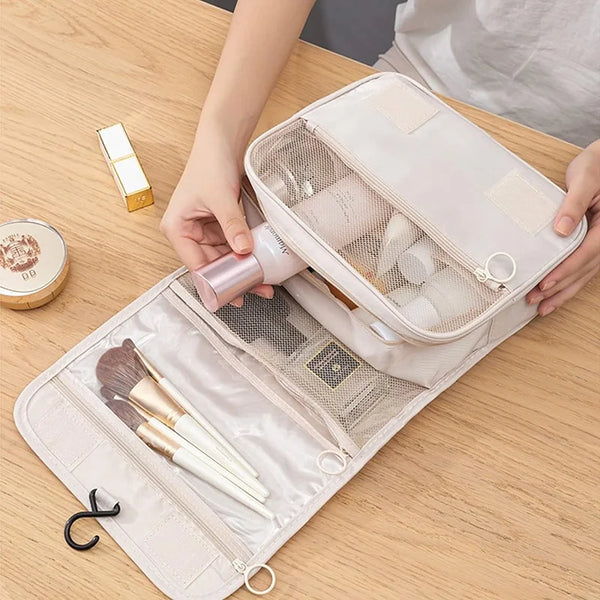 A light pink portable travel toiletries organizer bag is open, showing various makeup and grooming tools inside.