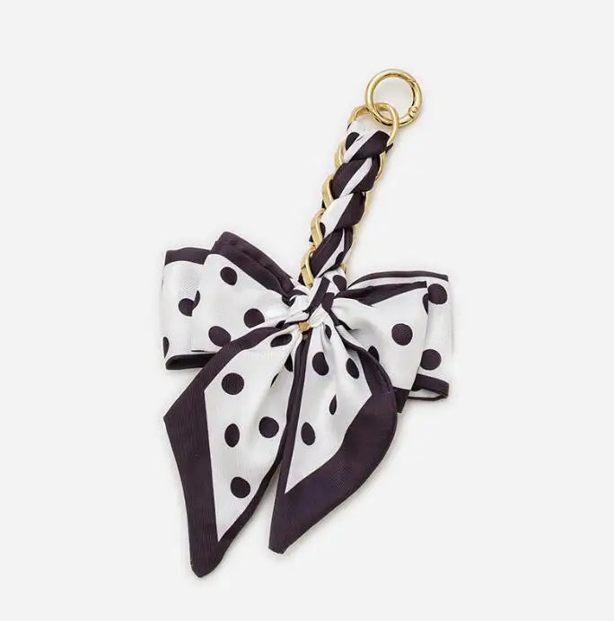 A black and white polka dot fabric bow with a gold chain strap extension for a handbag.