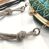 A close-up of a crystal rhinestone handbag chain strap featuring textured links and knot details against a green background.
