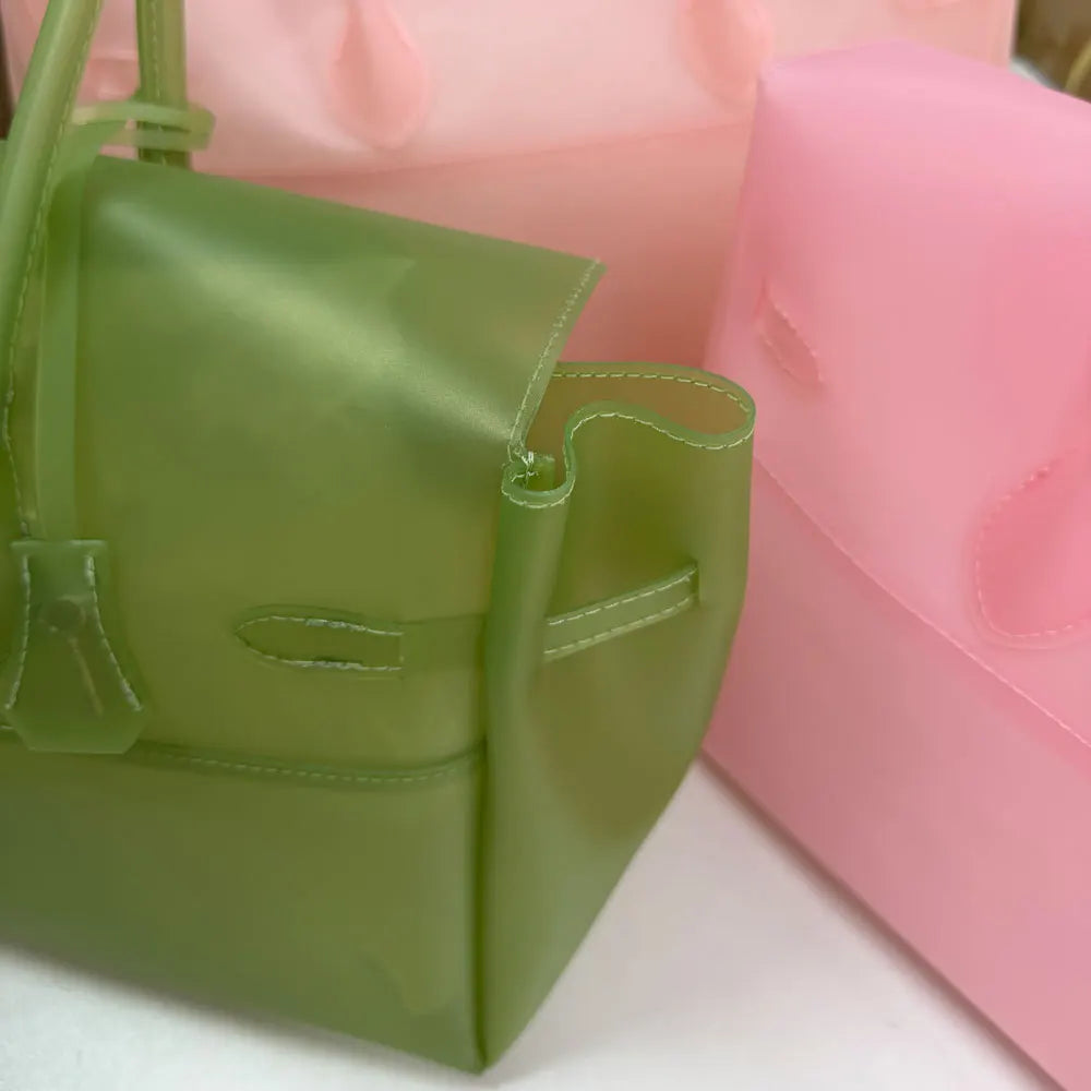 Un sac fourre-tout en gelée vert lime à côté d'une boîte de rangement en plastique rose.