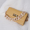 A light beige acrylic resin detachable bag chain strap is draped across a tan leather clutch resting on a white fluffy surfac