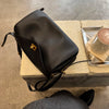 A black genuine leather square shoulder crossbody bag resting on a light-colored surface next to a coffee cup.