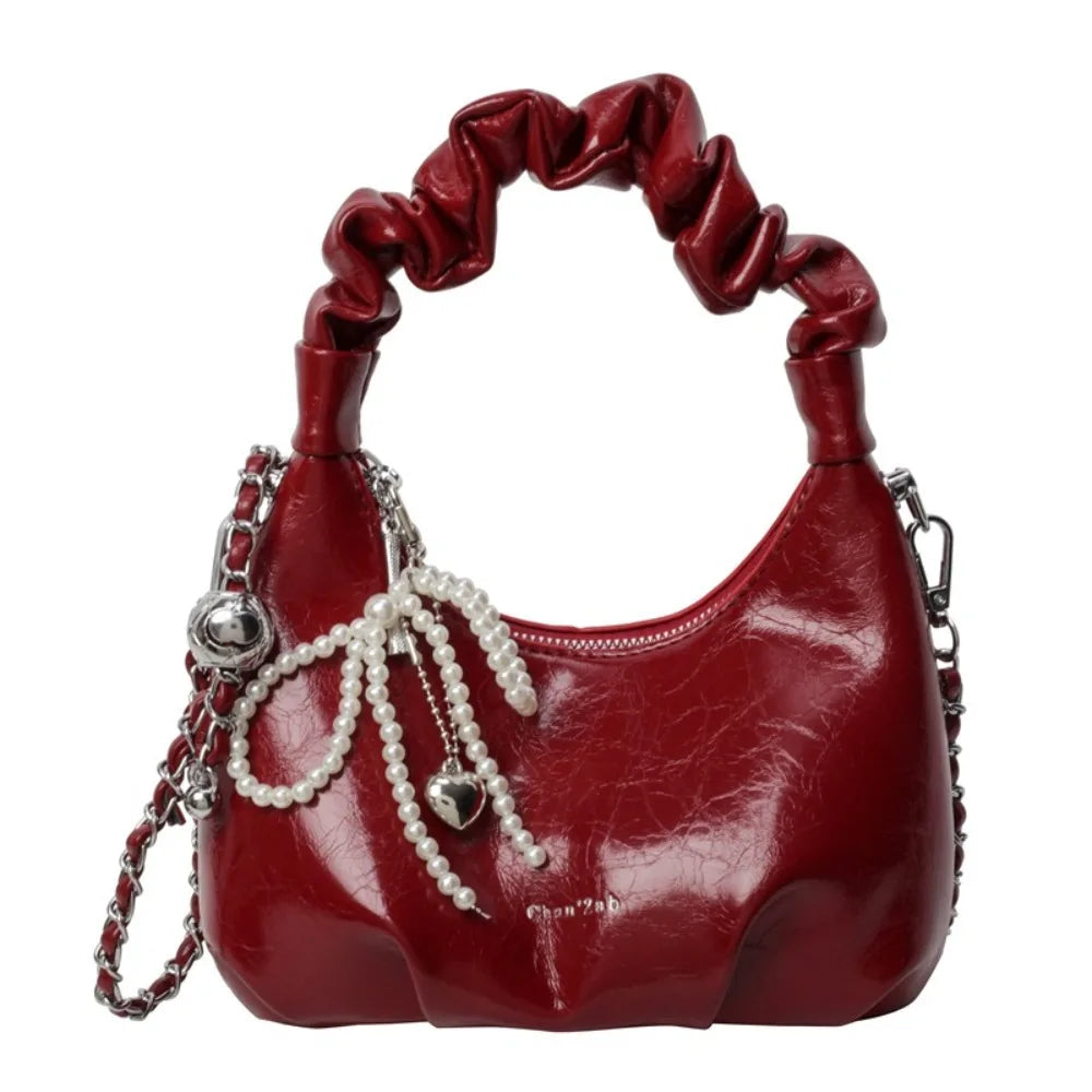 Clutch de cuero rojo intenso con detalle de lazo y acentos de cadena plateada.