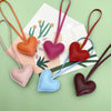 A collection of five heart-shaped PU leather keychains in various shades of pink, red, purple, blue, and brown on a light gre