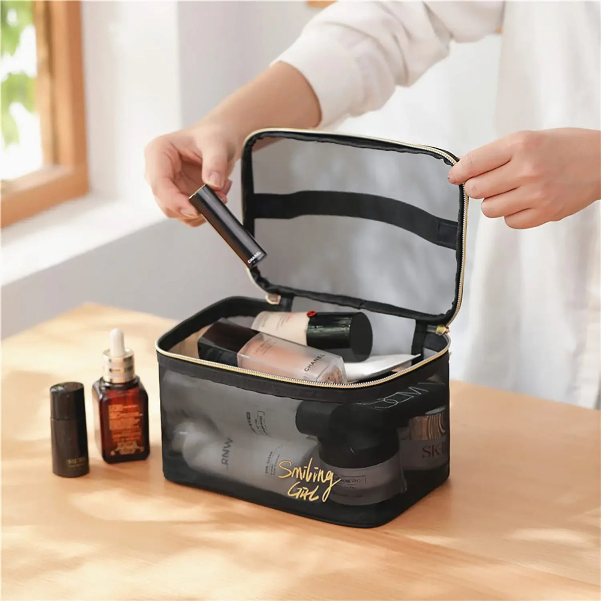 A hand opens a large capacity black mesh travel cosmetic storage pouch to reveal various makeup and skincare products.