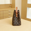 A brown leather bucket bag with a floral pattern and a tan adjustable strap resting on a light wood surface.