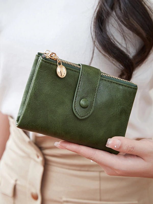 A hand holds a dark olive green minimalist card holder wallet with gold hardware against a light background.