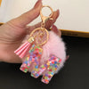 A gold-colored keychain featuring a pink fluffy pom-pom and a resin pendant shaped like the letter I.