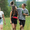 A woman and a man are walking through a field of tall green grass and wildflowers.