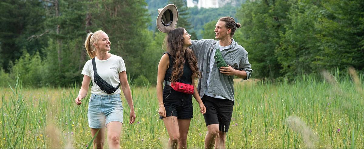 A woman and a man are walking through a field of tall green grass and wildflowers.