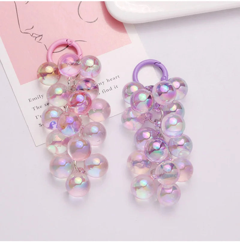 Un par de llaveros de uva de acrílico iridiscente rosa con anillos morados.