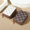 A pair of zippered card holder wallets, one white patterned and one dark brown patterned, resting on a beige surface.
