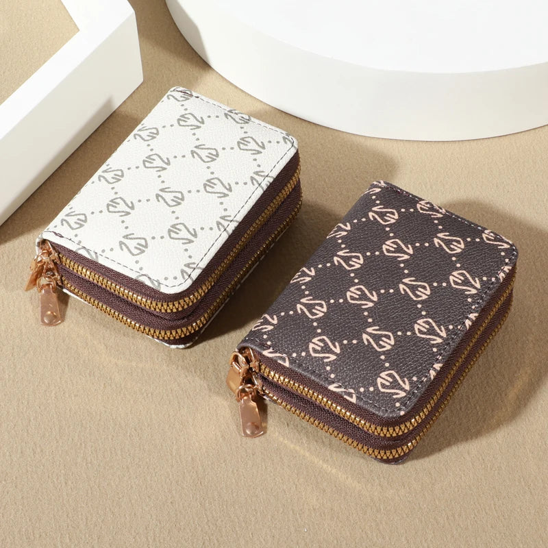 A pair of zippered card holder wallets, one white patterned and one dark brown patterned, resting on a beige surface.
