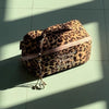 Bolsa de maquillaje para viajar con estampado de leopardo marrón sobre una superficie de baldosas verde claro.
