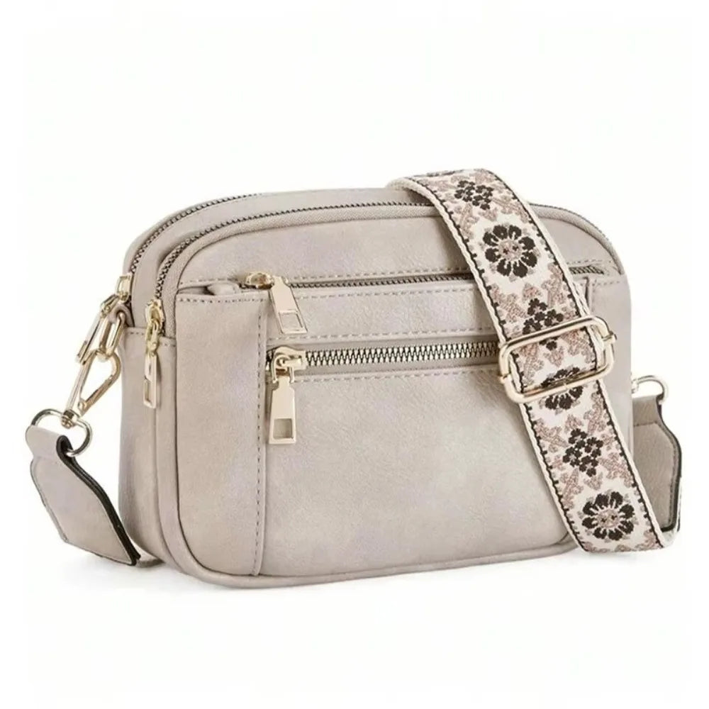 A light gray PU leather crossbody bag with a patterned strap and gold hardware.