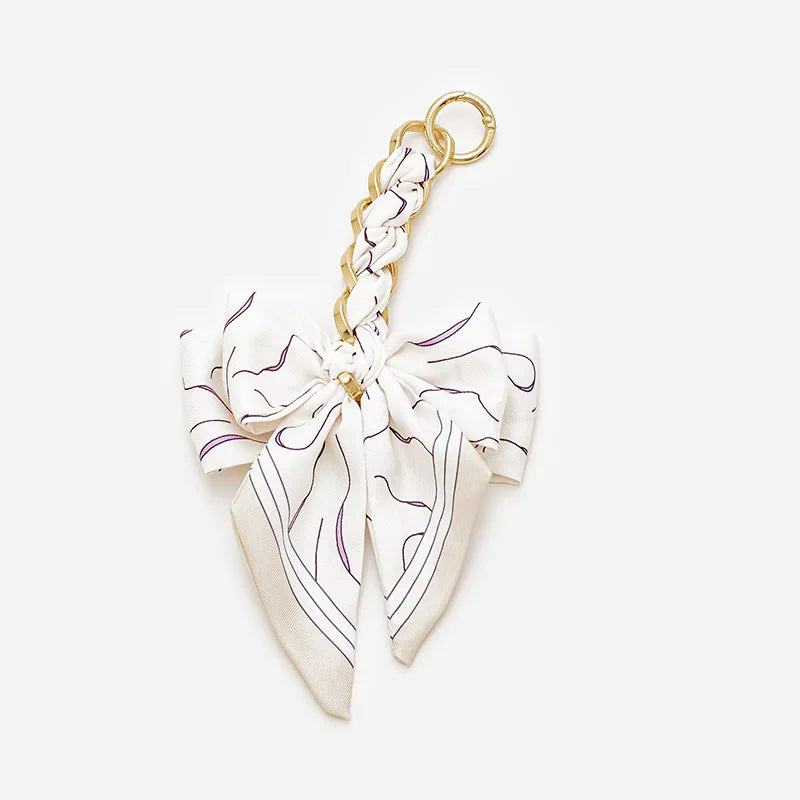 A white and purple patterned fabric bow attached to a gold-toned adjustable strap.