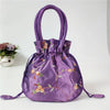 Clutch de noche con lazo brillante morado y bordado floral sobre una superficie blanca.