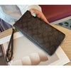 A dark brown monogrammed leather wallet with a gold zipper is shown resting on a light-colored surface.