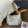 A light beige plaid nylon drawstring tote bag resting on a wooden surface next to a white pillow.