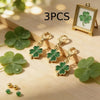 Three gold-toned four leaf clover keychains displayed on a wooden surface with a framed clover.