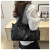 A woman is holding a black leather everyday large-capacity shoulder tote bag against a light wooden surface.