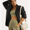 Eine Frau modelliert ein olivgrünes Crop-Top und passende Leggings mit einem schwarzen Blazer und einer beigen Crossbody-Tasc