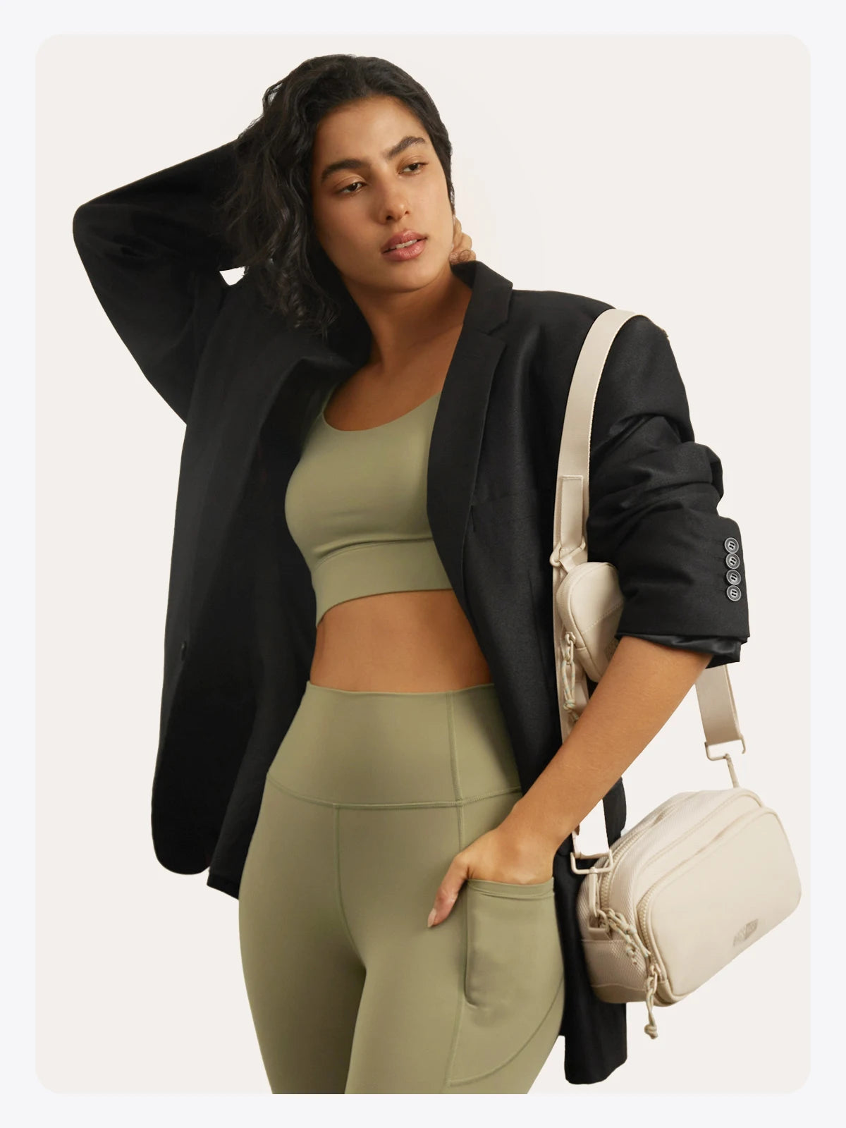 Eine Frau modelliert ein olivgrünes Crop-Top und passende Leggings mit einem schwarzen Blazer und einer beigen Crossbody-Tasc