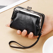 A black vintage PU leather compact wallet with a silver clasp and leather strap is held in a hand.
