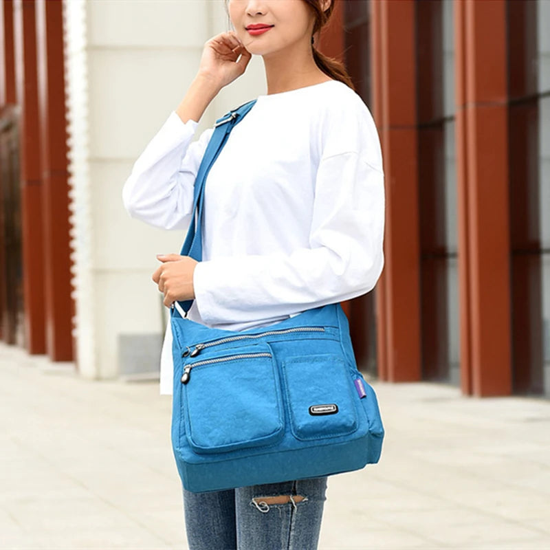 Eine Frau in weißem Oberteil und Jeans trägt eine blaue wasserdichte Nylon-Crossbody-Tasche.