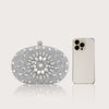 Pochette à clochette de strass et boîte, exposée à côté d'un smartphone blanc.