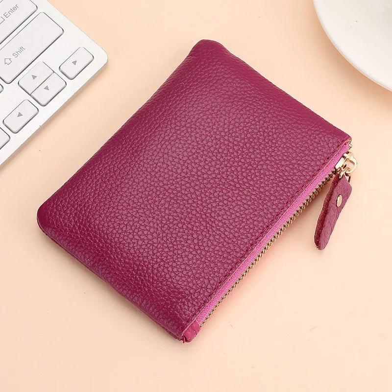 A deep magenta genuine leather mini zipper coin and card purse resting on a light beige surface next to a white keyboard.