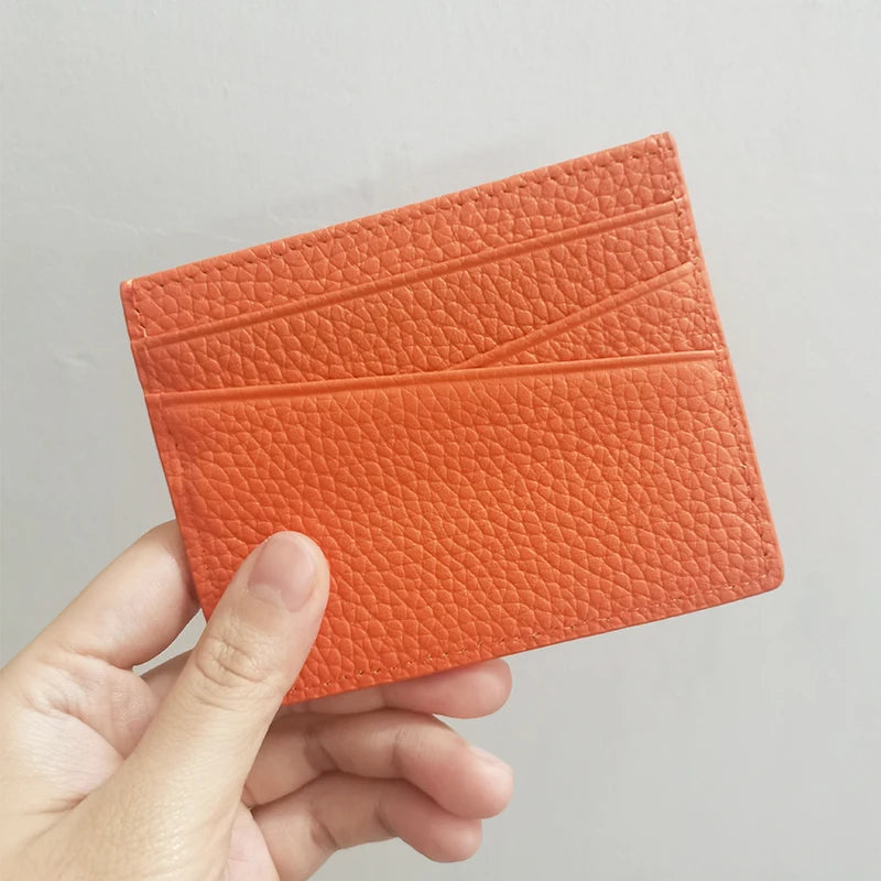 Une main tient un porte-cartes en cuir véritable orange à surface texturée.