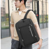 A young man wearing a beige shirt and dark pants is carrying a black nylon travel backpack.