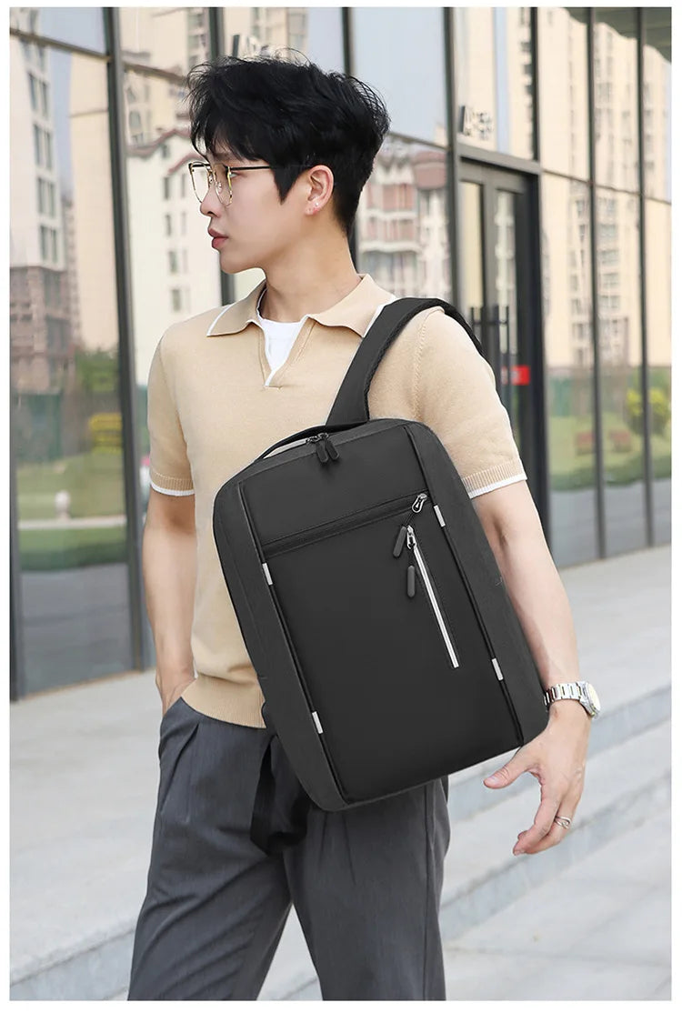 A young man wearing a beige shirt and dark pants is carrying a black nylon travel backpack.