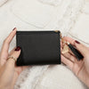 A hand holds a black PU leather coin clutch wallet with a gold chain and tassel.