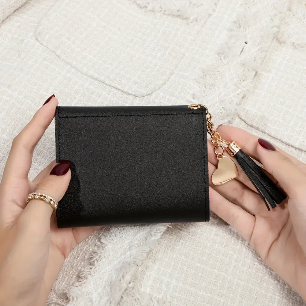 A hand holds a black PU leather coin clutch wallet with a gold chain and tassel.