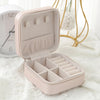 A light pink compact leather jewelry travel box is open, displaying multiple compartments for storing small items.