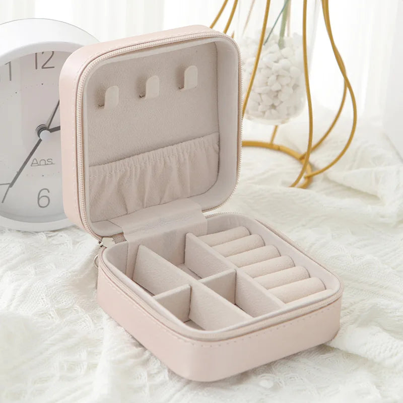 A light pink compact leather jewelry travel box is open, displaying multiple compartments for storing small items.
