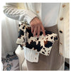 A hand holds a beige leopard print faux leather wrist bag against a white knitted sweater and tan skirt.