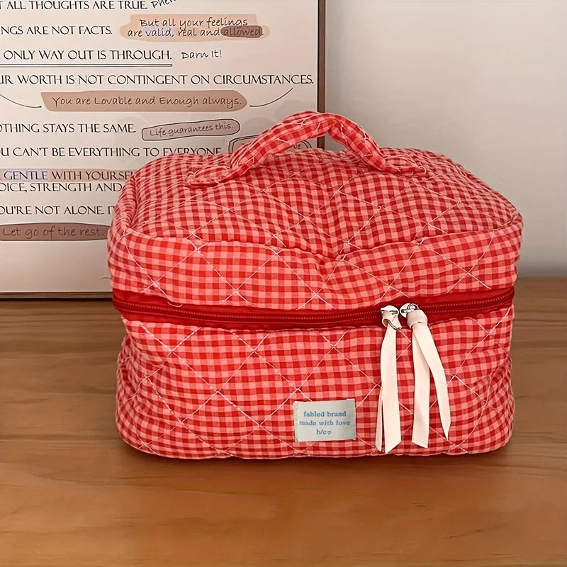 A red and white plaid cosmetic storage bag with a zipper and fabric ties is displayed on a wooden surface.