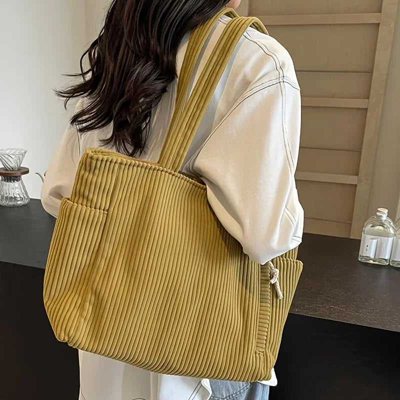 A light yellow corduroy casual handbag carried by a person, shown from the back and side.
