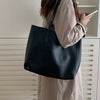 A woman holds a large black leather tote bag while standing in front of white slatted furniture.