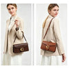 A woman models a brown leather shoulder bag with gold hardware and a beige blazer and white skirt.