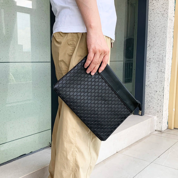 A woman holds a black quilted PU leather clutch bag in her hand outside a glass door.
