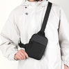 Un hombre con chaqueta blanca lleva un bolso cruzado negro impermeable sujeto a su camisa.