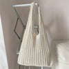 A cream-colored bohemian knit shoulder bag hanging on a metal rack.