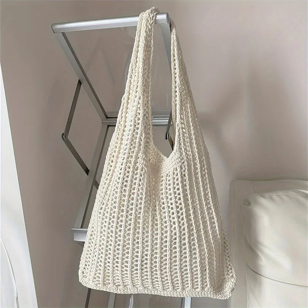 Sac à épaule en tricot bohème de couleur crème, suspendu sur un rack métallique.