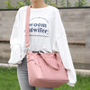 A person is holding a pink nylon tote bag with a zipper closure against a blurred outdoor background.